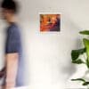 A man walking past a wall with a painting hanging on it.