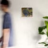 A man walking past a wall with a picture hanging on it.