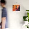 A man walking past a wall with a painting hanging on it.