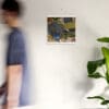 A man walking past a wall with a picture hanging on it.