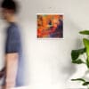 A man is walking past a painting on the wall.